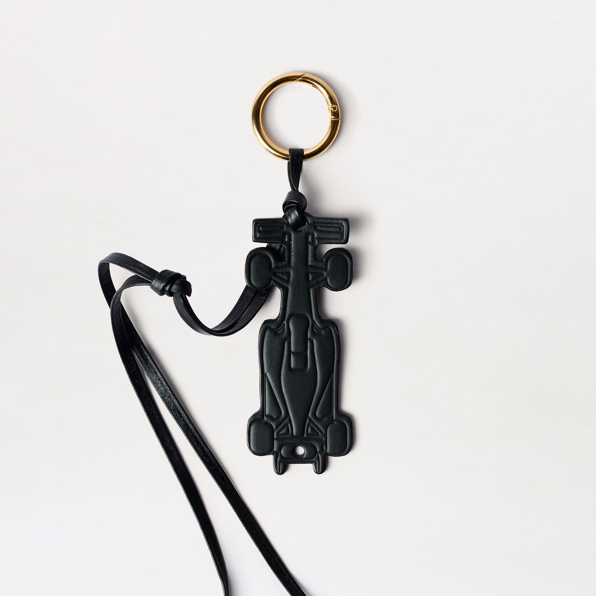 A black leather keychain shaped like a Formula 1 race car, featuring a gold-tone split keyring and a black leather strap, shown on a clean white background.