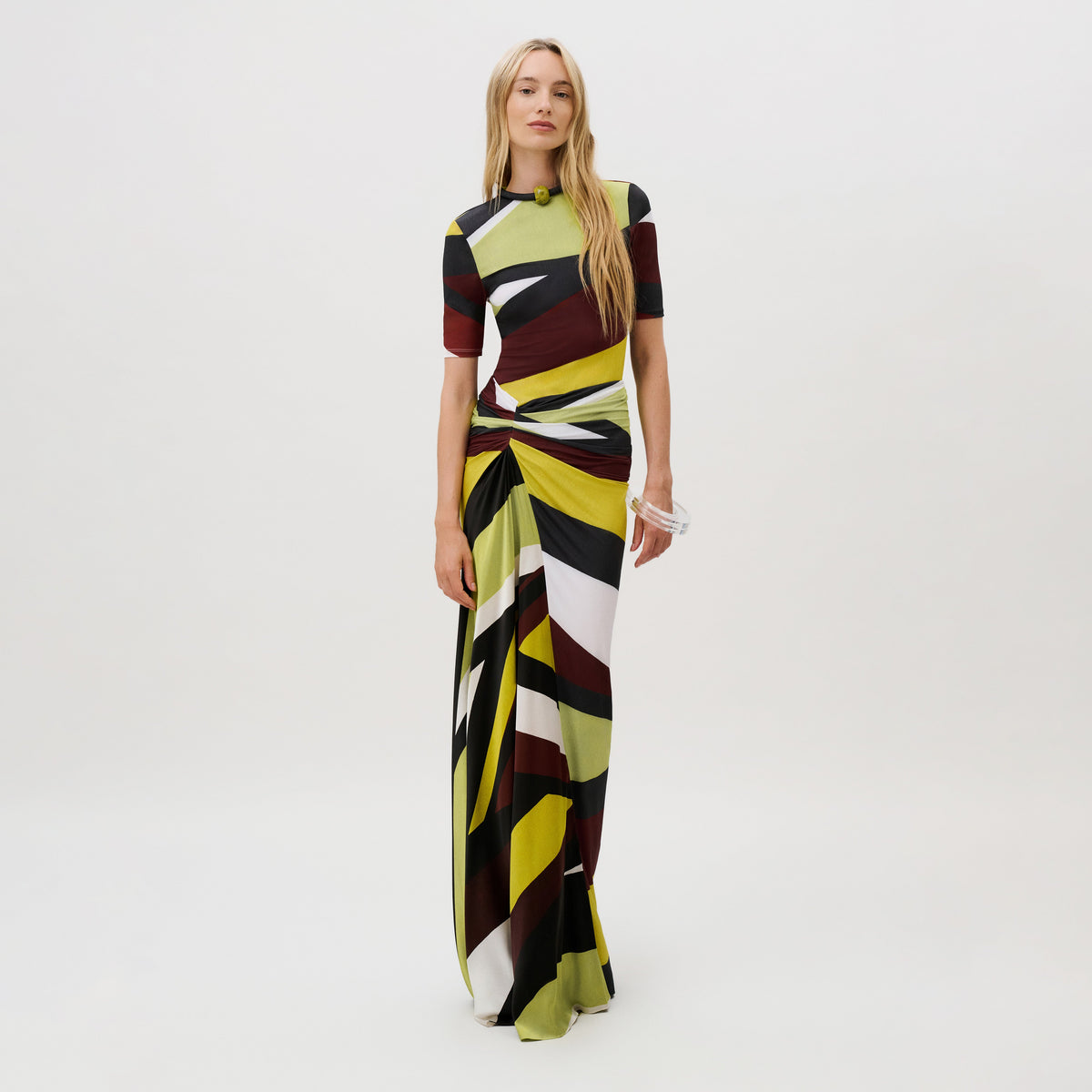 A model wears the Claudia Skirt, a floor-length, slim-fit skirt in Italian fabric featuring a geometric, multicolored abstract print and a gathered, draped waist detail.