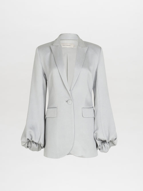 Introducing the Coco Blazer Gray by Silvia Tcherassi, featuring a single-button closure, two pockets, and bubble sleeves with elasticized cuffs. Made from luxurious hammered satin with a subtle sheen, this elegant piece adds sophistication to any ensemble.