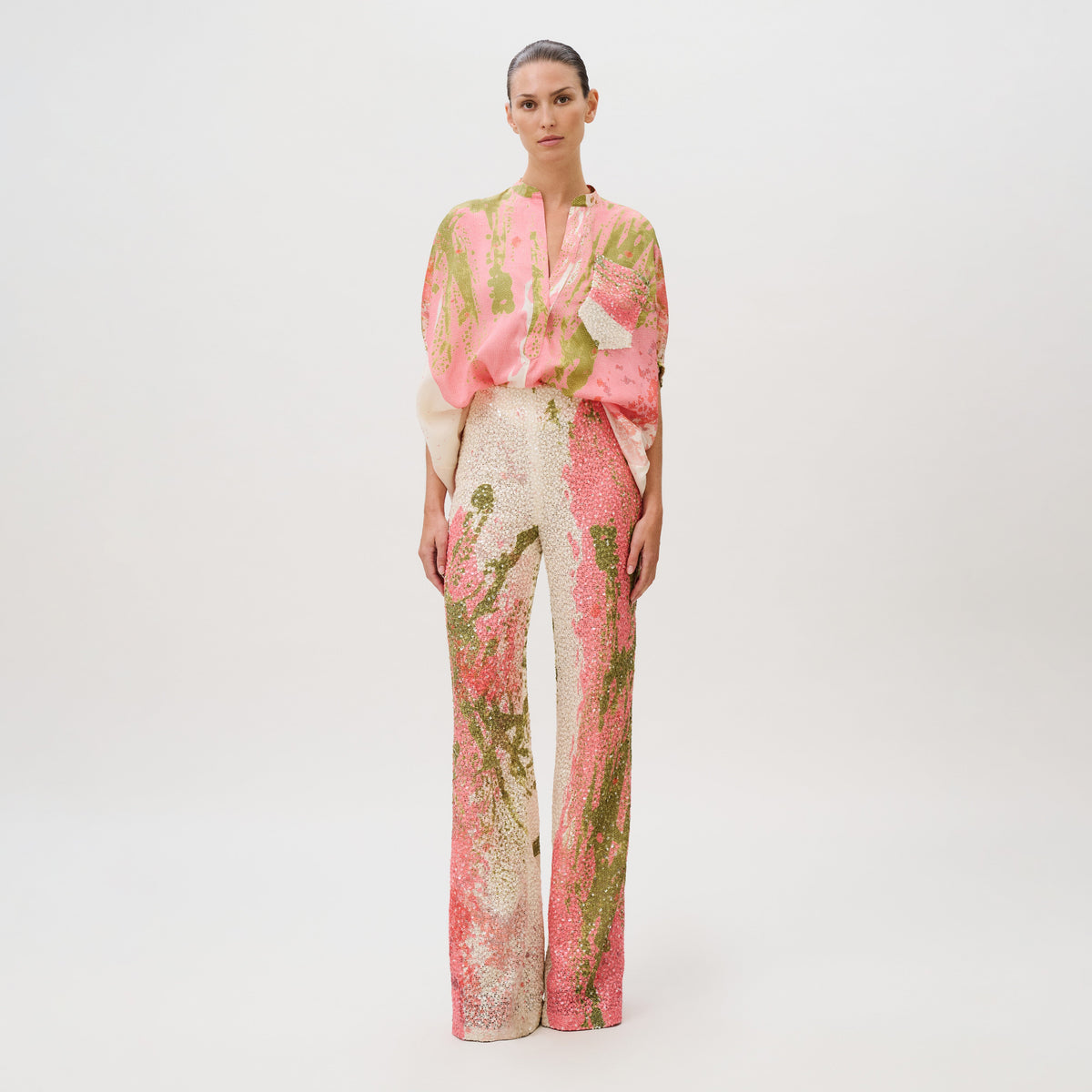 A model wearing a pink and green abstract-print blouse and matching Como Pant wide-leg sequin trousers made in Colombia.