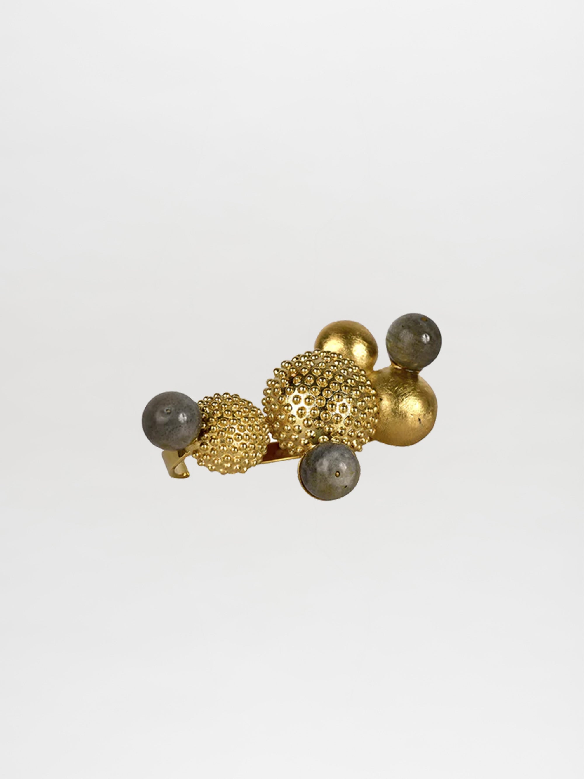 The Coral Ring by SilviaTcherassiEU features gold and gray spheres—some smooth, others with textured bumps—set against a white background, making it a stylish accent to order.