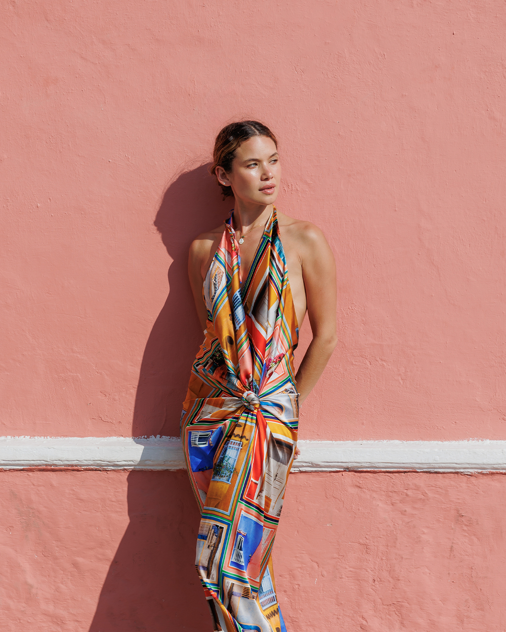 Woman wearing a colorful patterned dress against a pink wall
