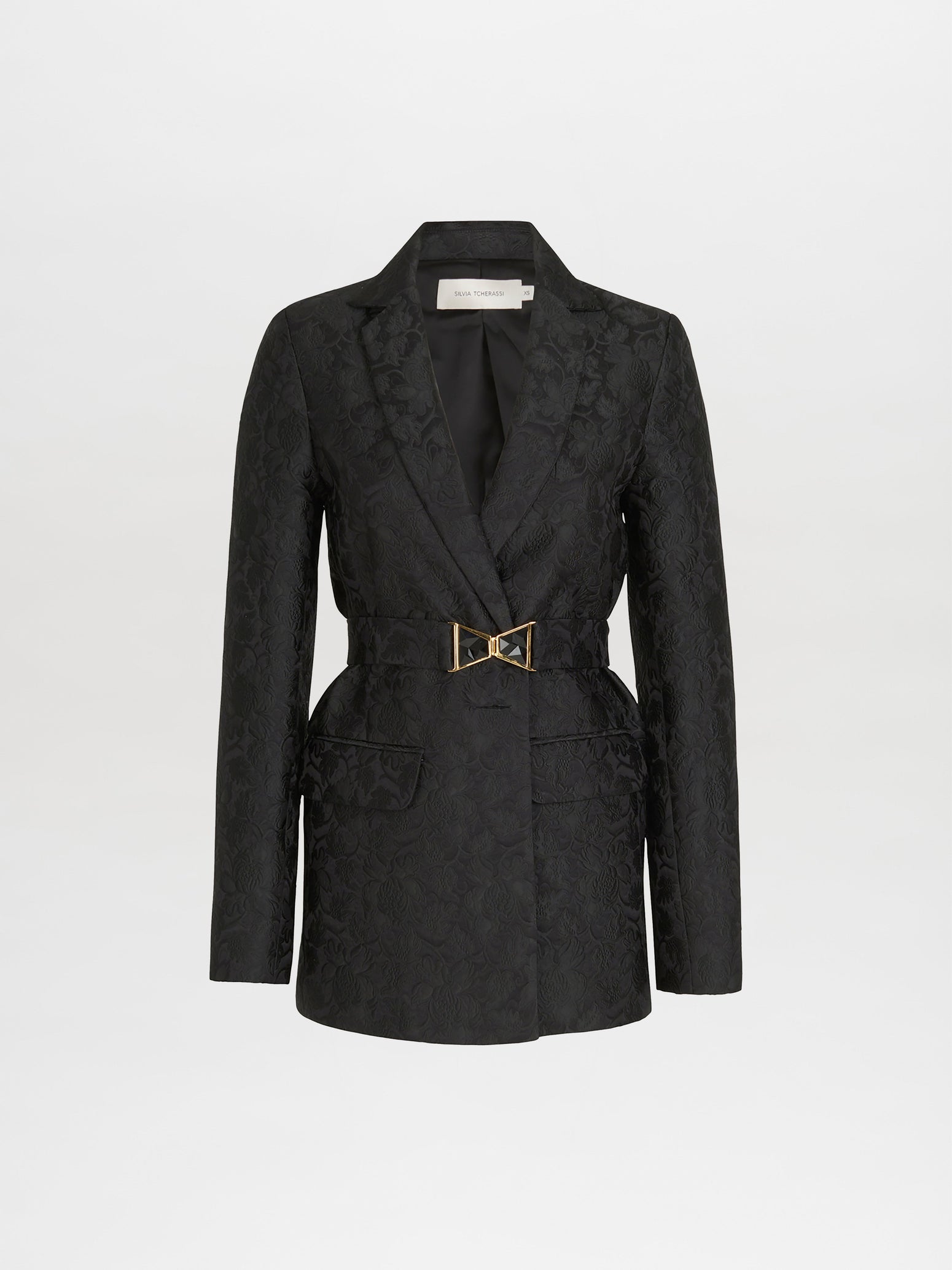 The Silvia Tcherassi Cuneo Jacket in black broccato jacquard features a notched lapel and button closure, highlighted by a gold-tone belt at the waist. Its classic tailoring pops against a plain light backdrop.