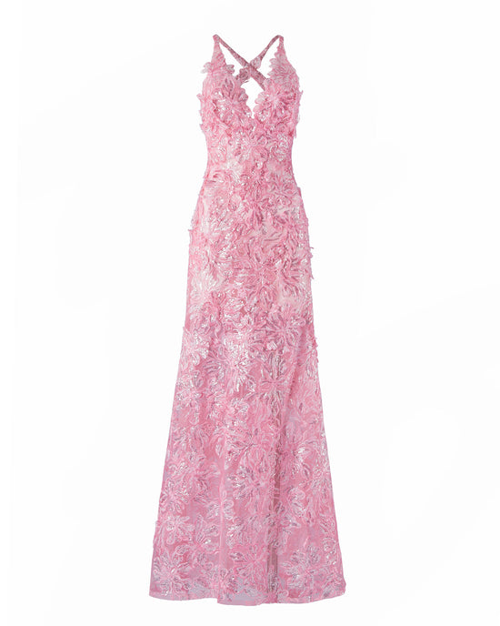 A person stands wearing the Daira Dress Pink, a long dress with thin straps and a beautiful floral pattern. The background is plain and light-colored. This elegant dress is now available for pre-order and will ship by February 1st, 2025.