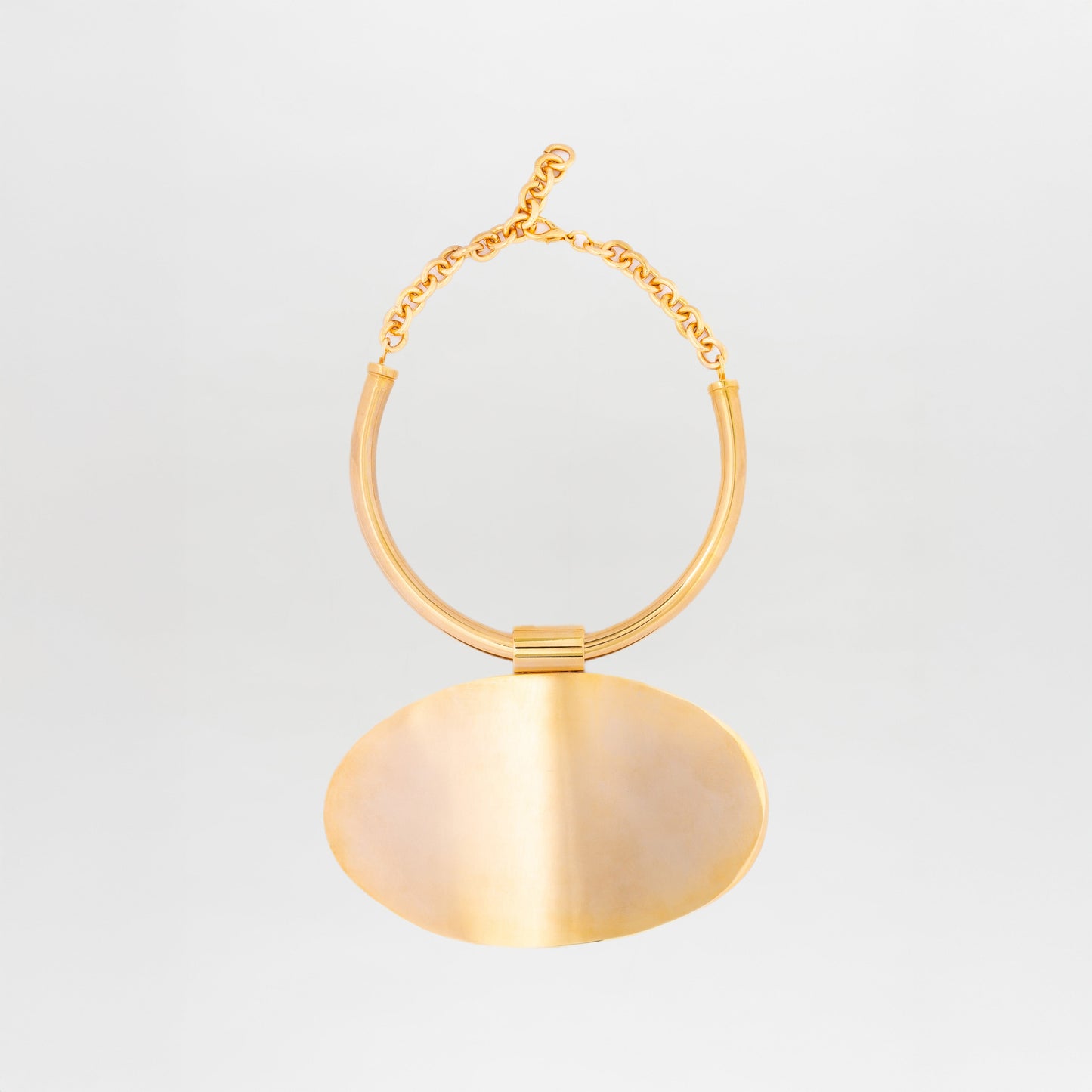 The Danielle Necklace by SVT DESIGNS features chunky twisted gold-plated brass links and a thick, oval pendant. Its smooth, shiny finish adds a minimalistic silhouette against a plain white background.