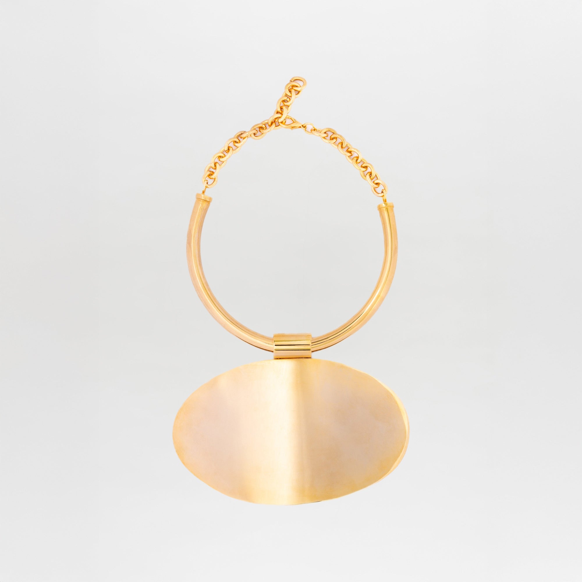 The Danielle Necklace by SVT DESIGNS features chunky twisted gold-plated brass links and a thick, oval pendant. Its smooth, shiny finish adds a minimalistic silhouette against a plain white background.