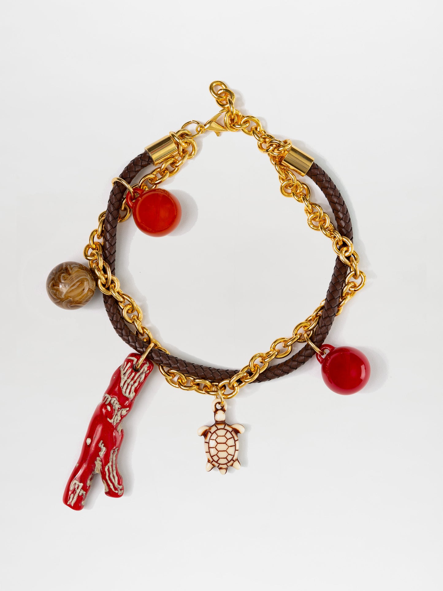 The Eira Necklace by SVT DESIGNS features gold links and a brown braided leather cord adorned with multicolor charms, including a red coral piece, a small gold turtle, two round red beads, and one patterned brown bead. This elegant piece is finished with a secure clasp closure.