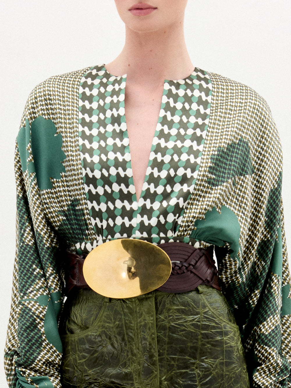 Person wearing a green patterned outfit with a gold belt on a white background