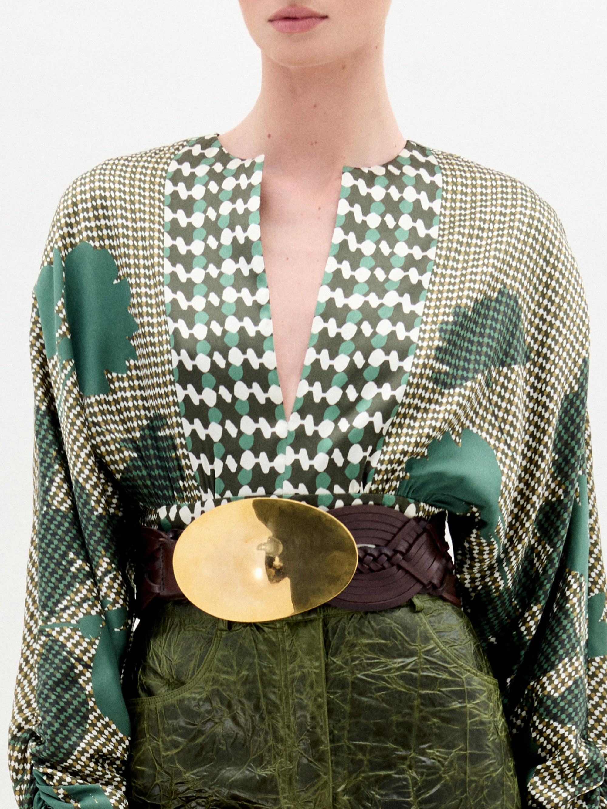 Person wearing a green patterned outfit with a gold belt on a white background
