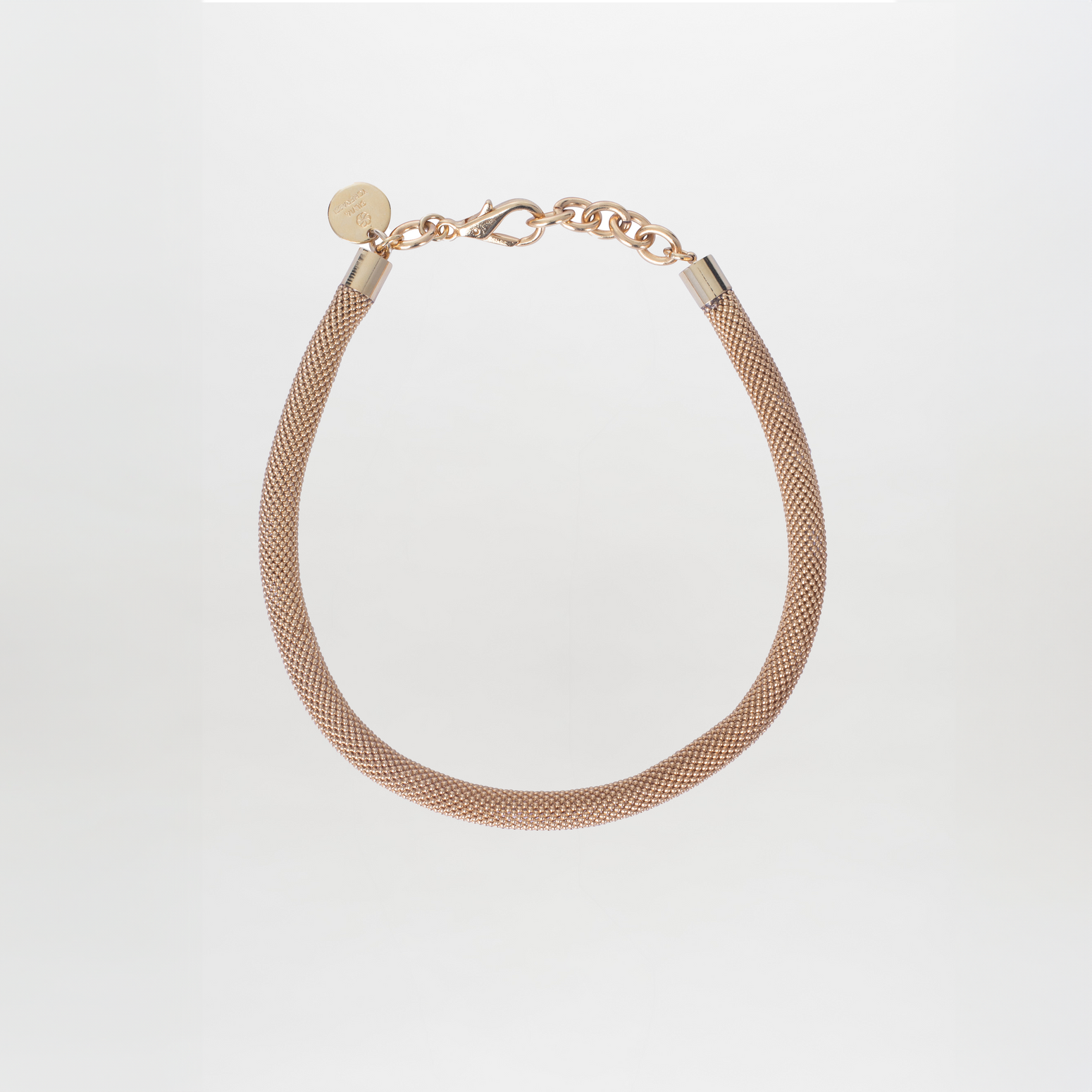 The Elara Necklace by SVT DESIGNS is a gold-plated brass chain piece with a textured design, featuring a chain clasp and round tag engraved with Tcherassi motifs, showcased elegantly on a plain white background.