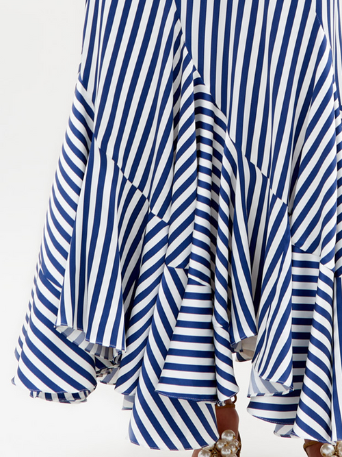 Close-up of the SVT DESIGNS Florina Skirt, a flowing high-waisted maxi featuring blue and white diagonal stripes. Crafted from Italian fabric, it has a layered mermaid silhouette with ruffles and beaded accents at the hem, partially revealing footwear.