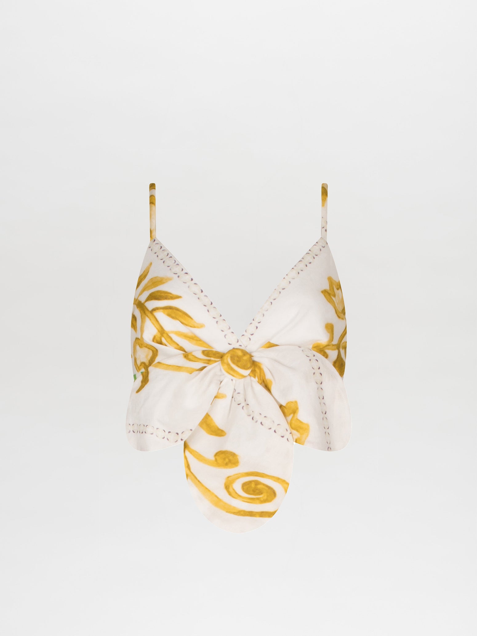 The Flor Top by Silvia Tcherassi US is a white halter top adorned with yellow floral and swirl patterns. It features 3D petal detailing, a central knot, and thin straps for an elegant look.