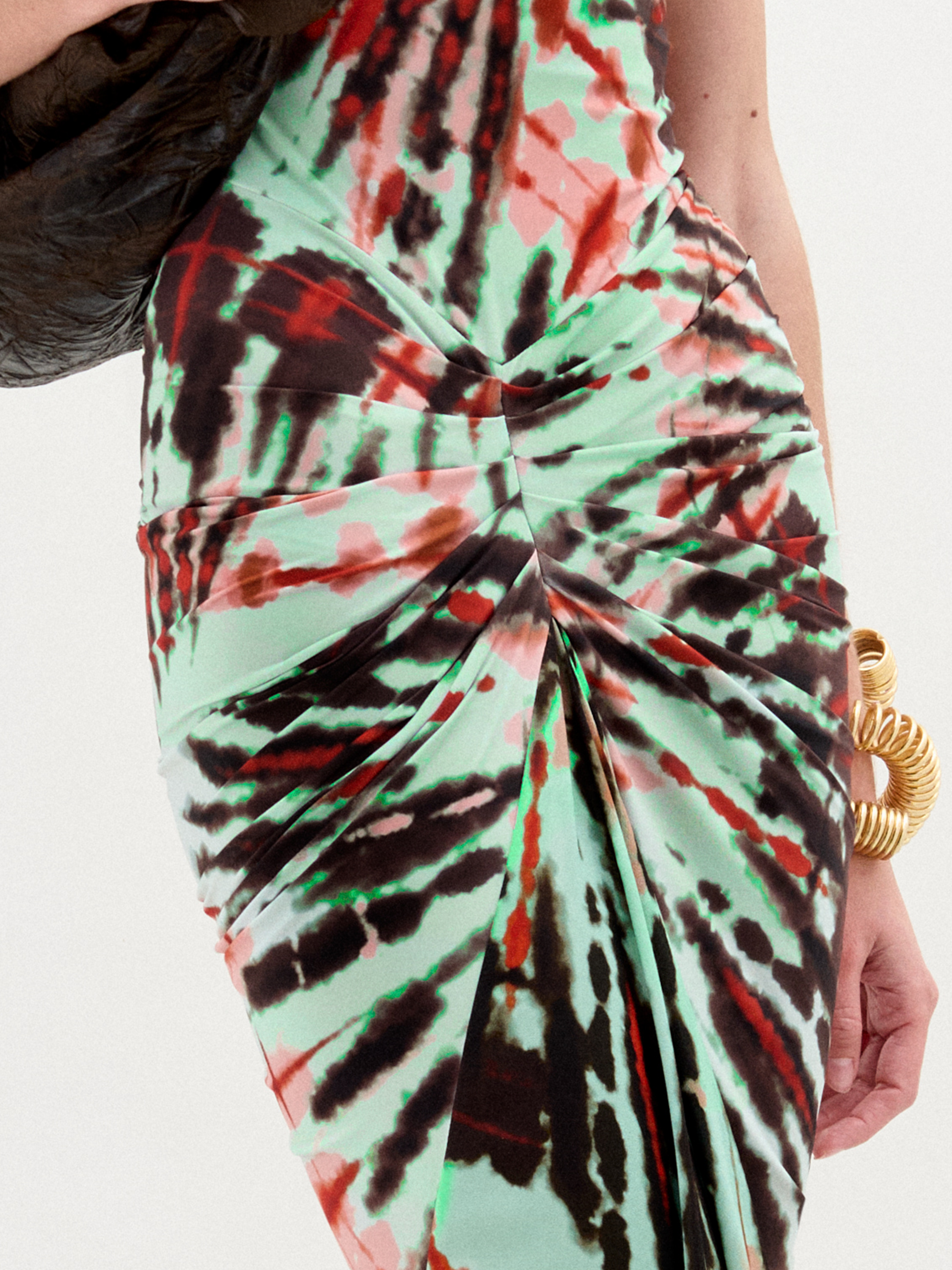 A woman wears the Frances Dress, a sleeveless, slim-fit maxi with a high neckline, holding a dark jacket over her shoulder against a plain white background.