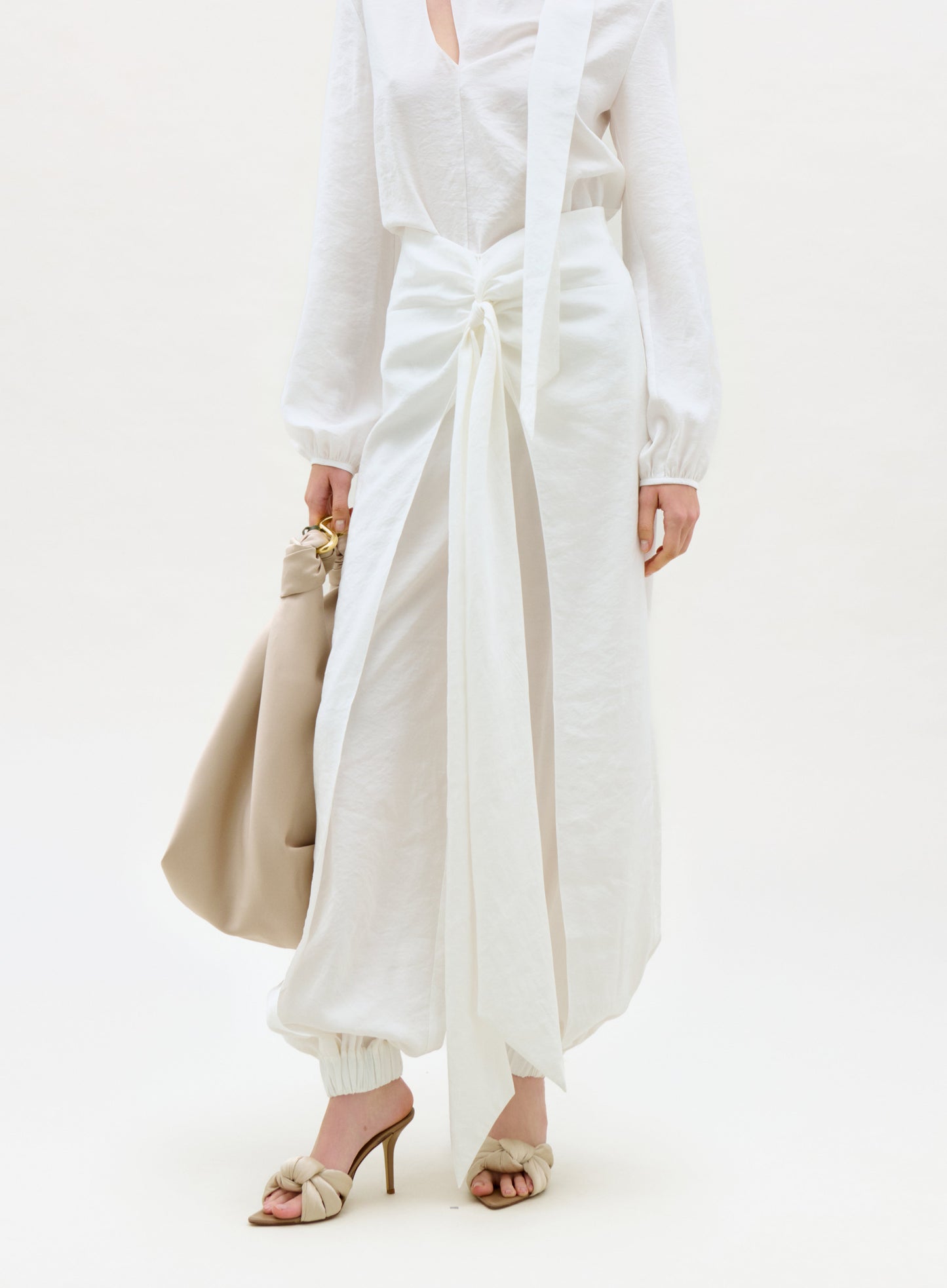 Person wearing a white outfit with wide-leg pants and holding a beige handbag on a white background