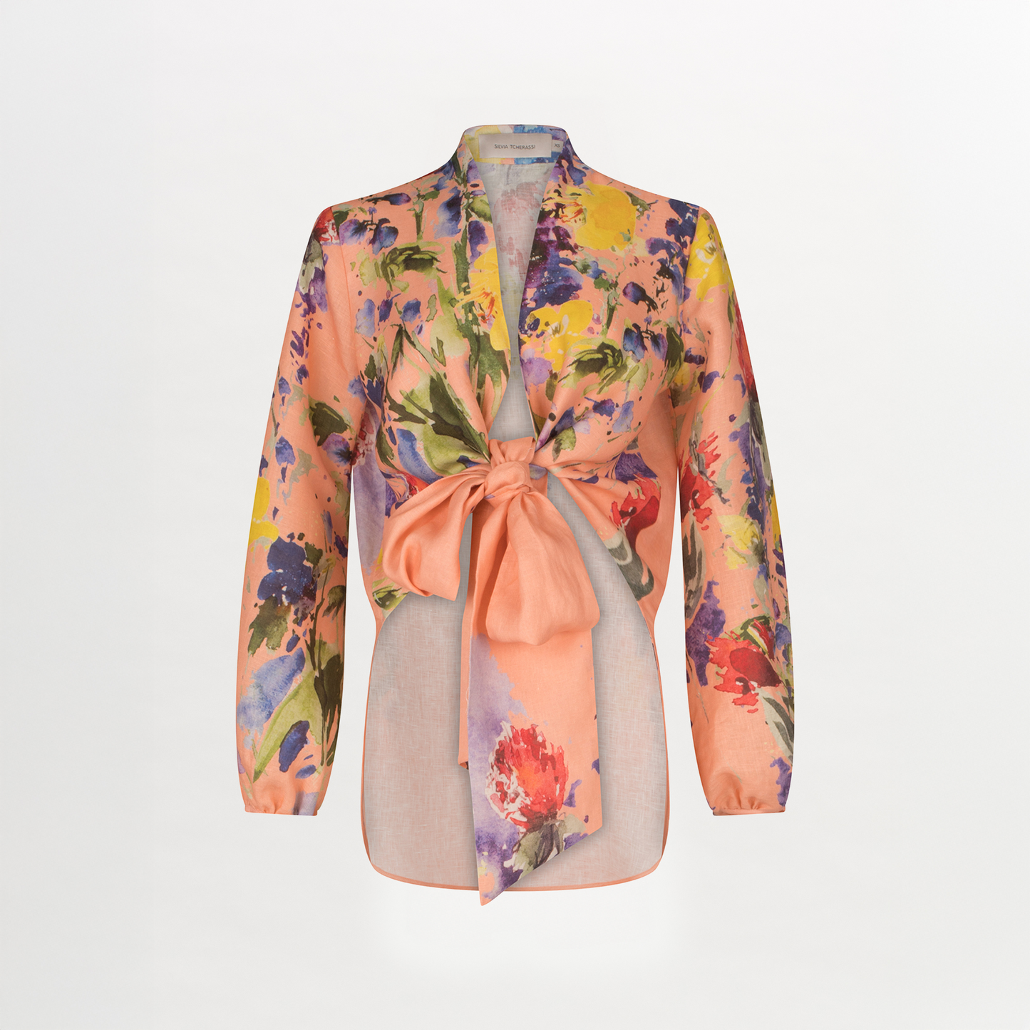 The Silvia Tcherassi US Floral Blouse features sheer, long-sleeved linen with a vibrant abstract floral print over peach, deep V neckline, large front waist tie, straight hem, and collar, shown on a plain white background.