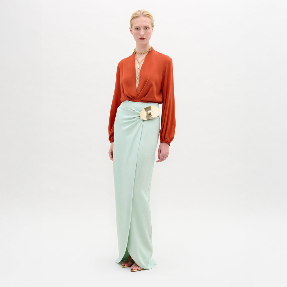 Woman wearing an orange blouse and light green skirt on a white background