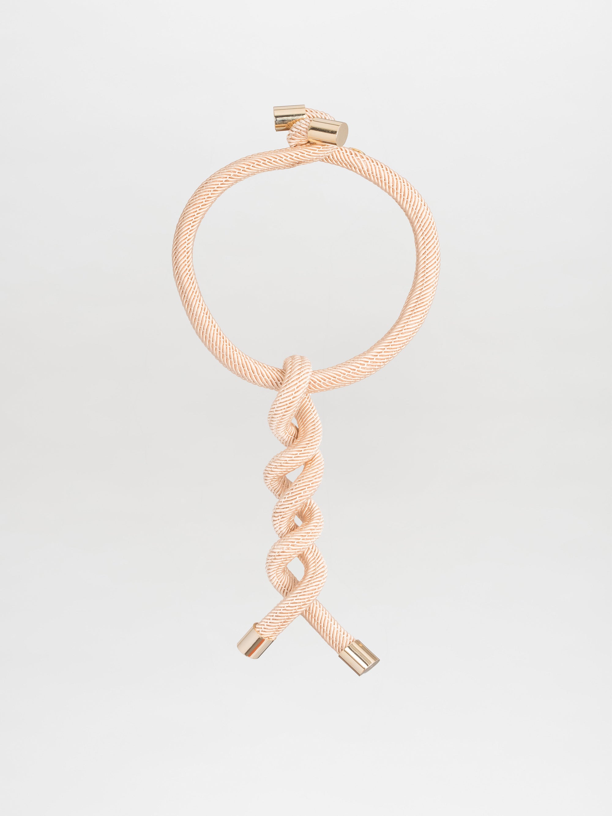 The Hazel Necklace by Silvia Tcherassi is a stunning cord-effect piece with intricate twist detailing, showcased against a plain backdrop. Its beige braids form a circle at the top, while the ends sparkle with metallic jewel-like accents.