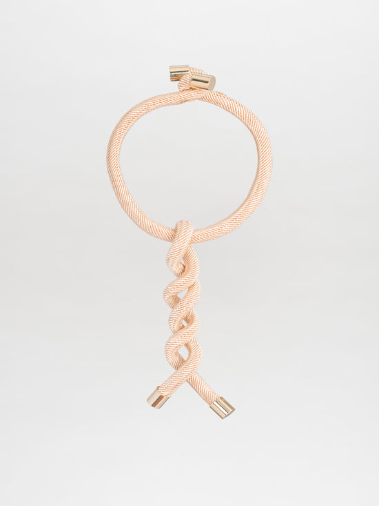 The Hazel Necklace by Silvia Tcherassi is a stunning cord-effect piece with intricate twist detailing, showcased against a plain backdrop. Its beige braids form a circle at the top, while the ends sparkle with metallic jewel-like accents.