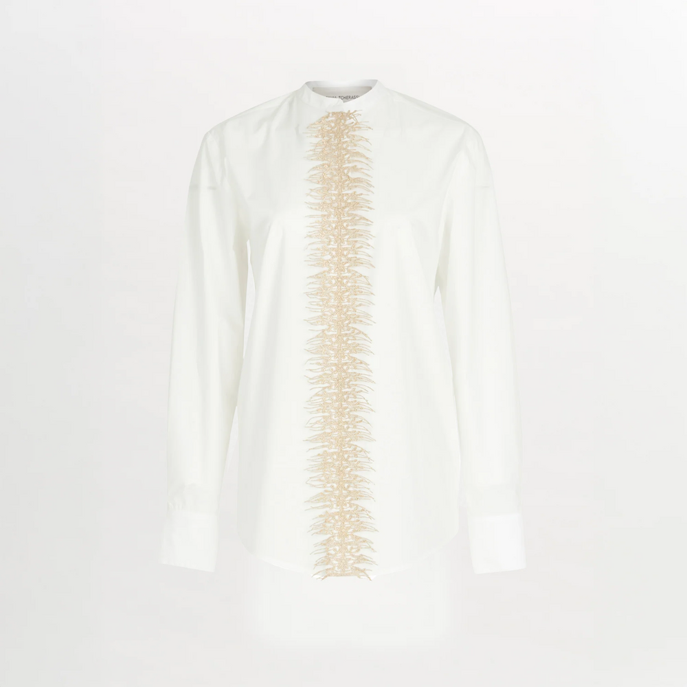 The Isabel Blouse White is a long-sleeve cotton poplin shirt with beige embroidery running vertically down the center front, set against a crisp white background.