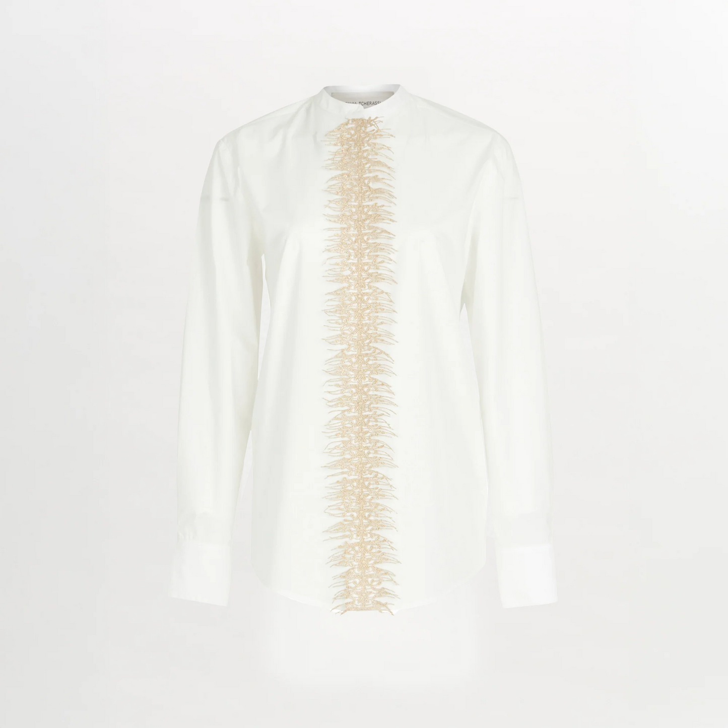 The Isabel Blouse White is a long-sleeve cotton poplin shirt with beige embroidery running vertically down the center front, set against a crisp white background.