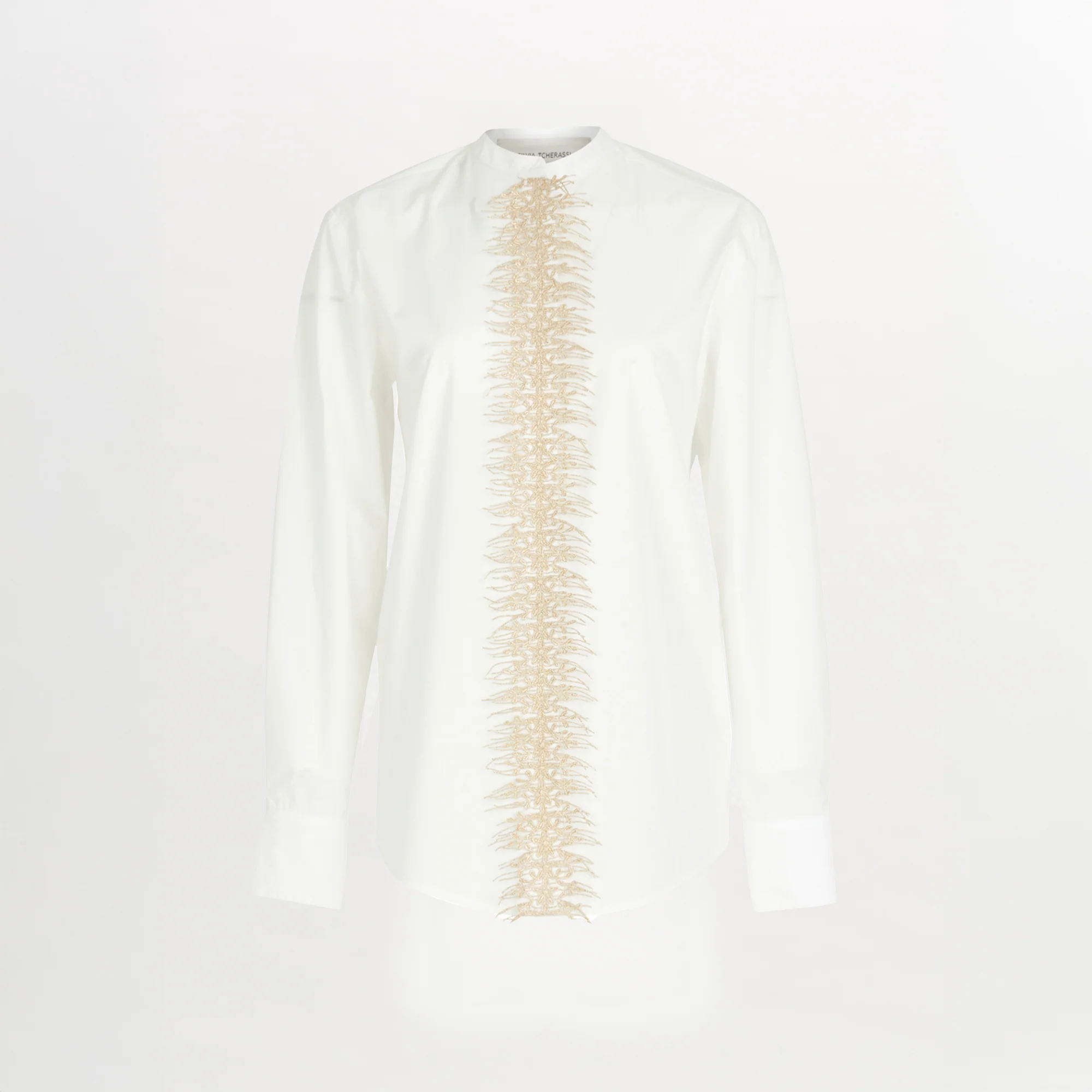 The Isabel Blouse White is a long-sleeve cotton poplin shirt with beige embroidery running vertically down the center front, set against a crisp white background.