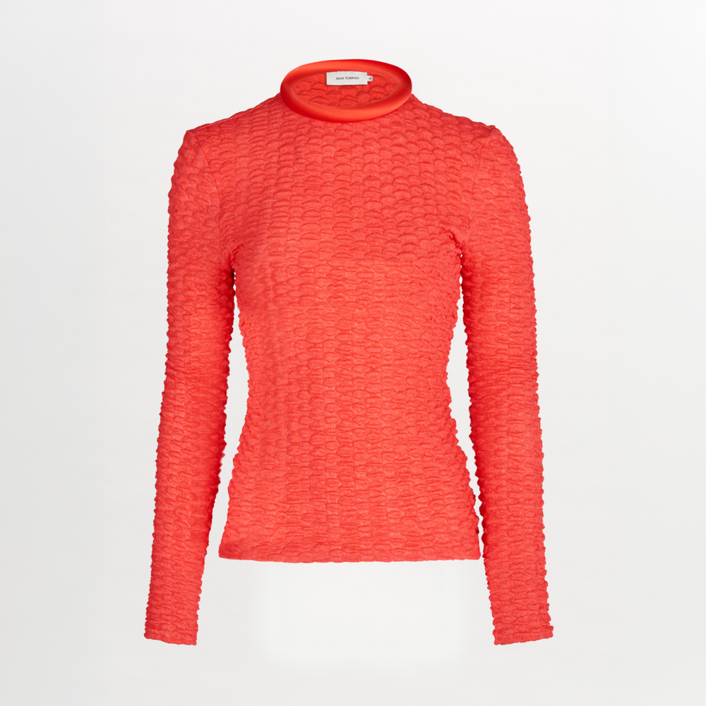 The Jari Top from Resort 2024 features a bright red embossed jacquard fabric, long sleeves, a fitted silhouette, mock turtleneck, and subtle circular pattern, displayed on a plain white background.