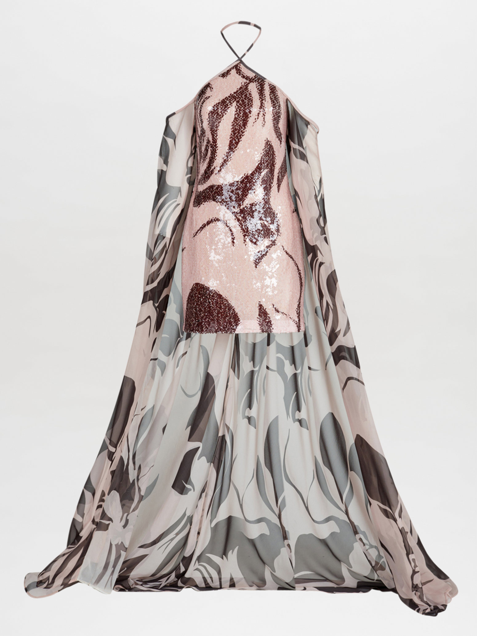 Silvia Tcherassi's Kavya Dress features a halter neckline with a pink sequined mini bodice adorned by an attached chiffon cape showcasing a marbled pattern in gray, black, and white. The open design elegantly reveals the sparkling dress underneath.