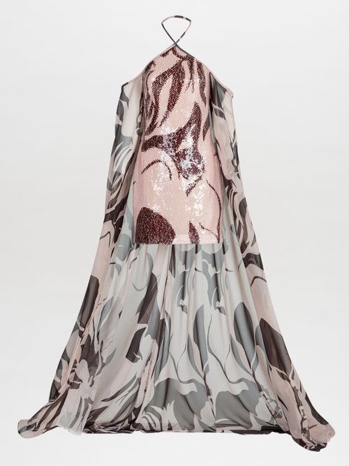 Silvia Tcherassi's Kavya Dress features a halter neckline with a pink sequined mini bodice adorned by an attached chiffon cape showcasing a marbled pattern in gray, black, and white. The open design elegantly reveals the sparkling dress underneath.