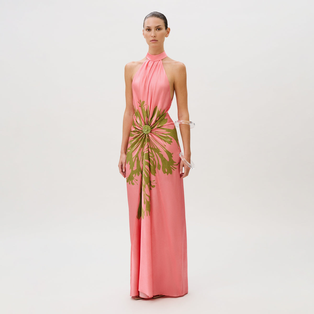 The Koori Dress is a floor-length pink silk halter dress featuring a green floral-like print gathered at the center waist.