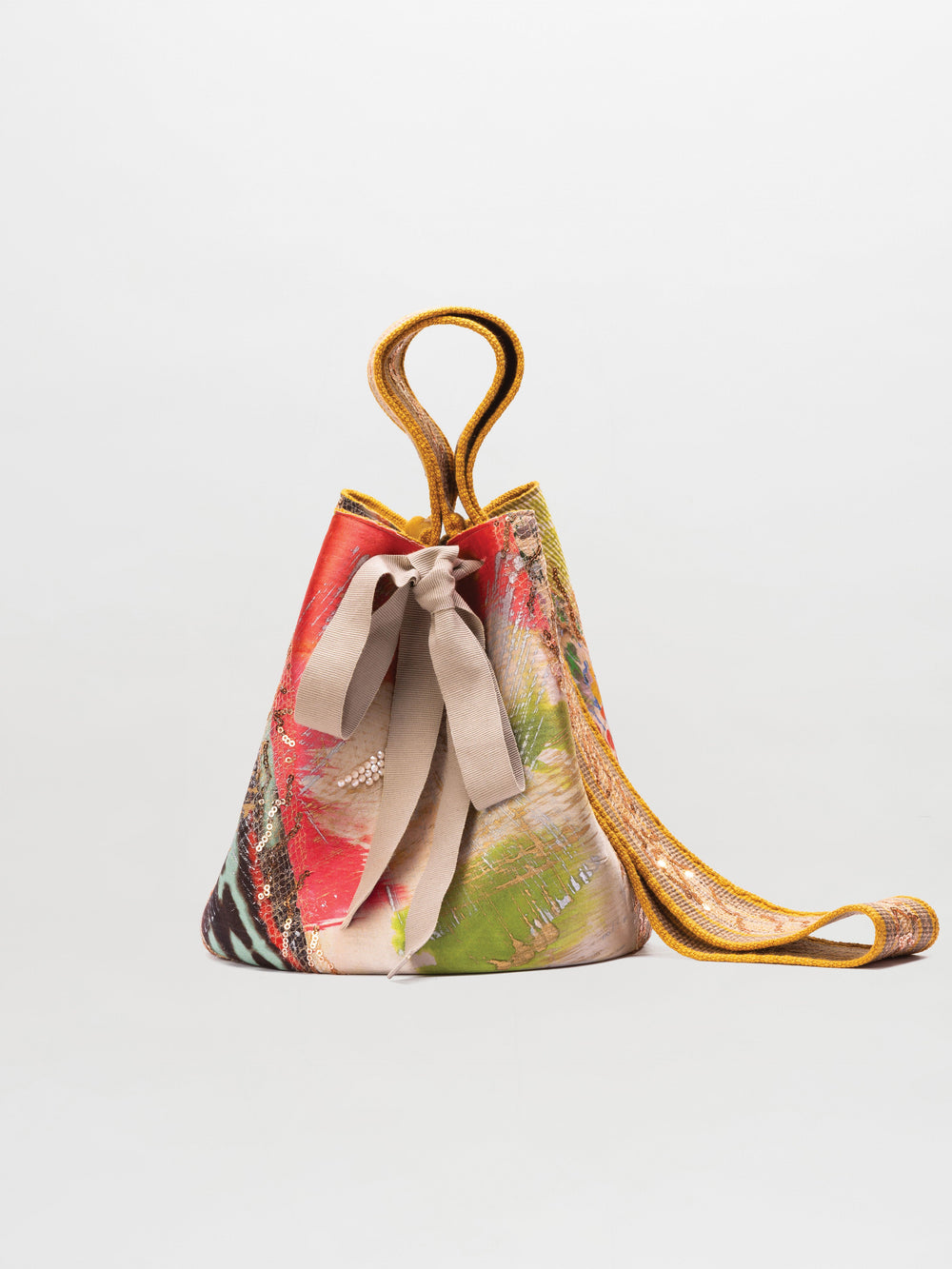 The Mochila Laaput Big by SVT DESIGNS is a multicolored patterned handbag with a beige drawstring closure and a long yellow hand-woven strap, displayed upright against a plain light gray background.