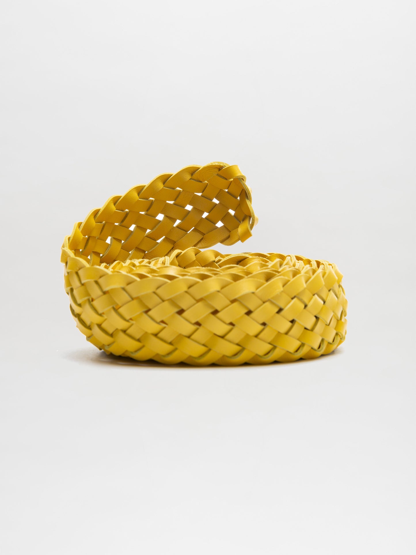 A coiled, yellow woven basket with an open top is showcased against a simple white background, emphasizing craftsmanship similar to the Lauren Belt by SVT DESIGNS inspired by braided Italian leather.