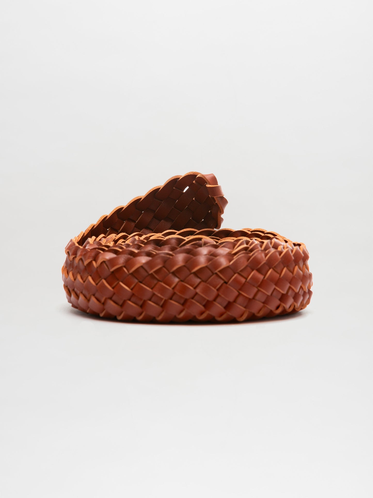 The Lauren Belt by SVT DESIGNS is a coiled brown braided belt made of Italian leather, set against a white background, highlighting its intricate craftsmanship and exquisite texture.