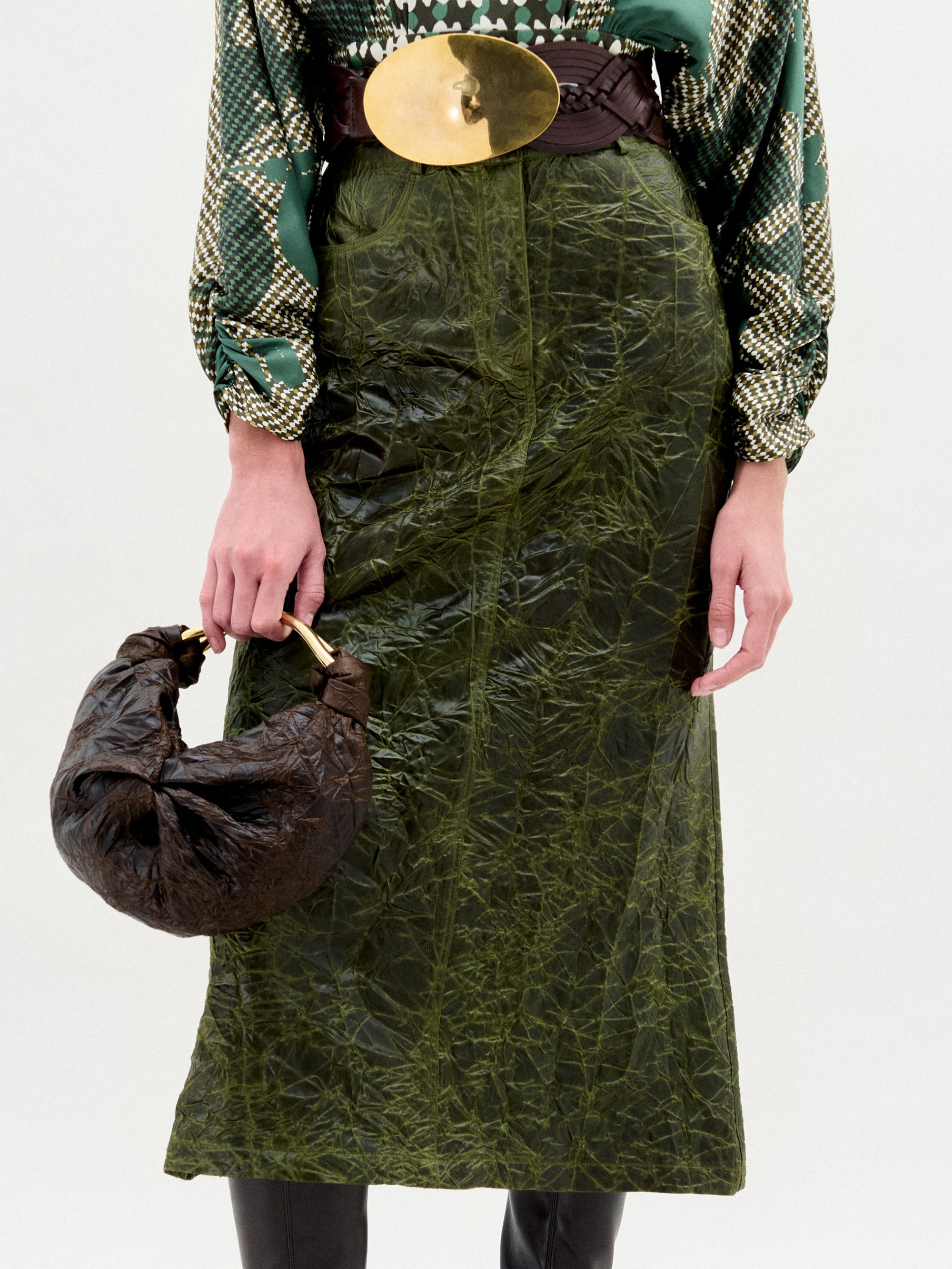 Person wearing a green patterned skirt and holding a brown bag on a white background