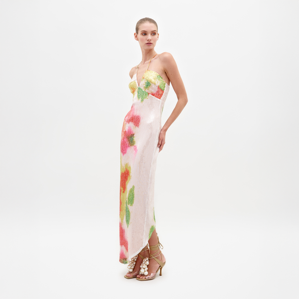 A woman is wearing the Lisseth Dress Spring Blooms, a strapless white dress adorned with colorful floral patterns, paired with high-heeled sandals featuring ankle straps and large pearl embellishments—an ideal choice for those who pre-order by February 15th to ensure timely shipping.