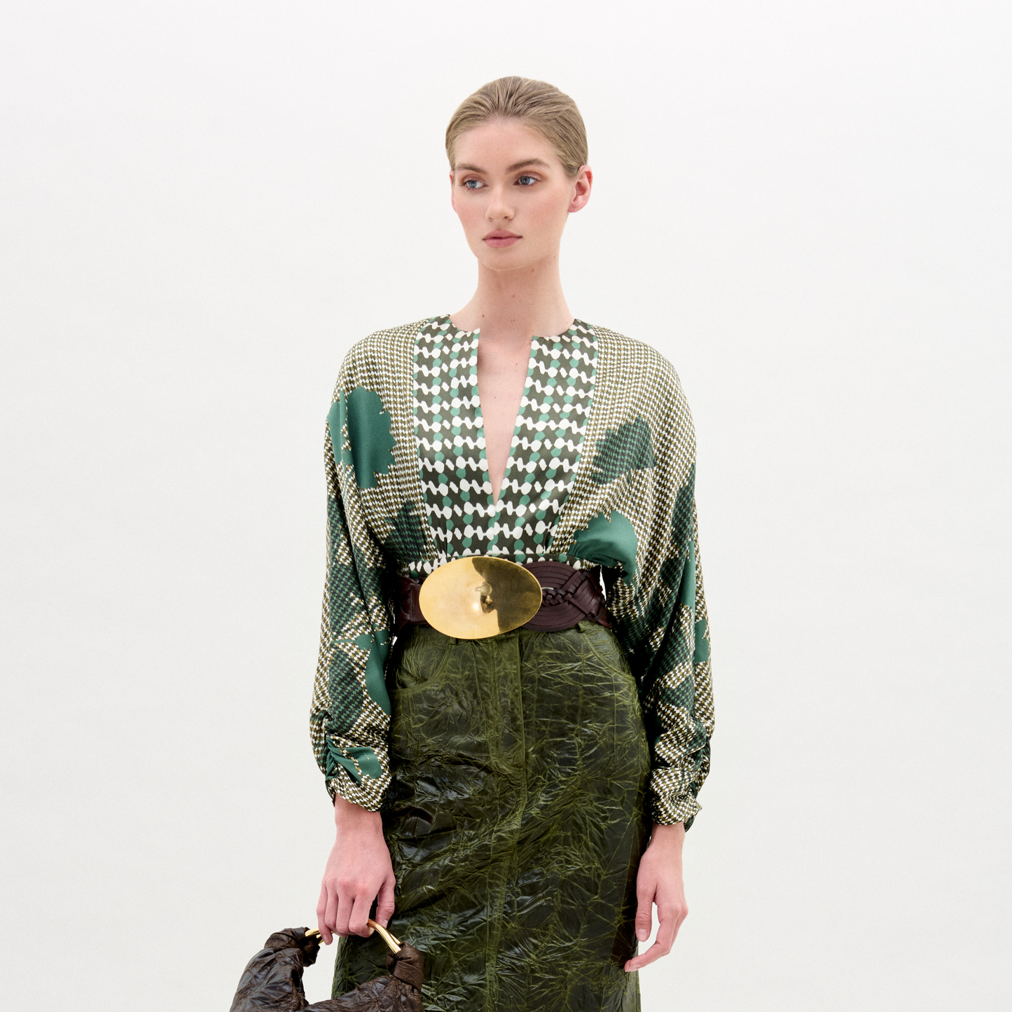 Model wearing a patterned top and green skirt with a white background