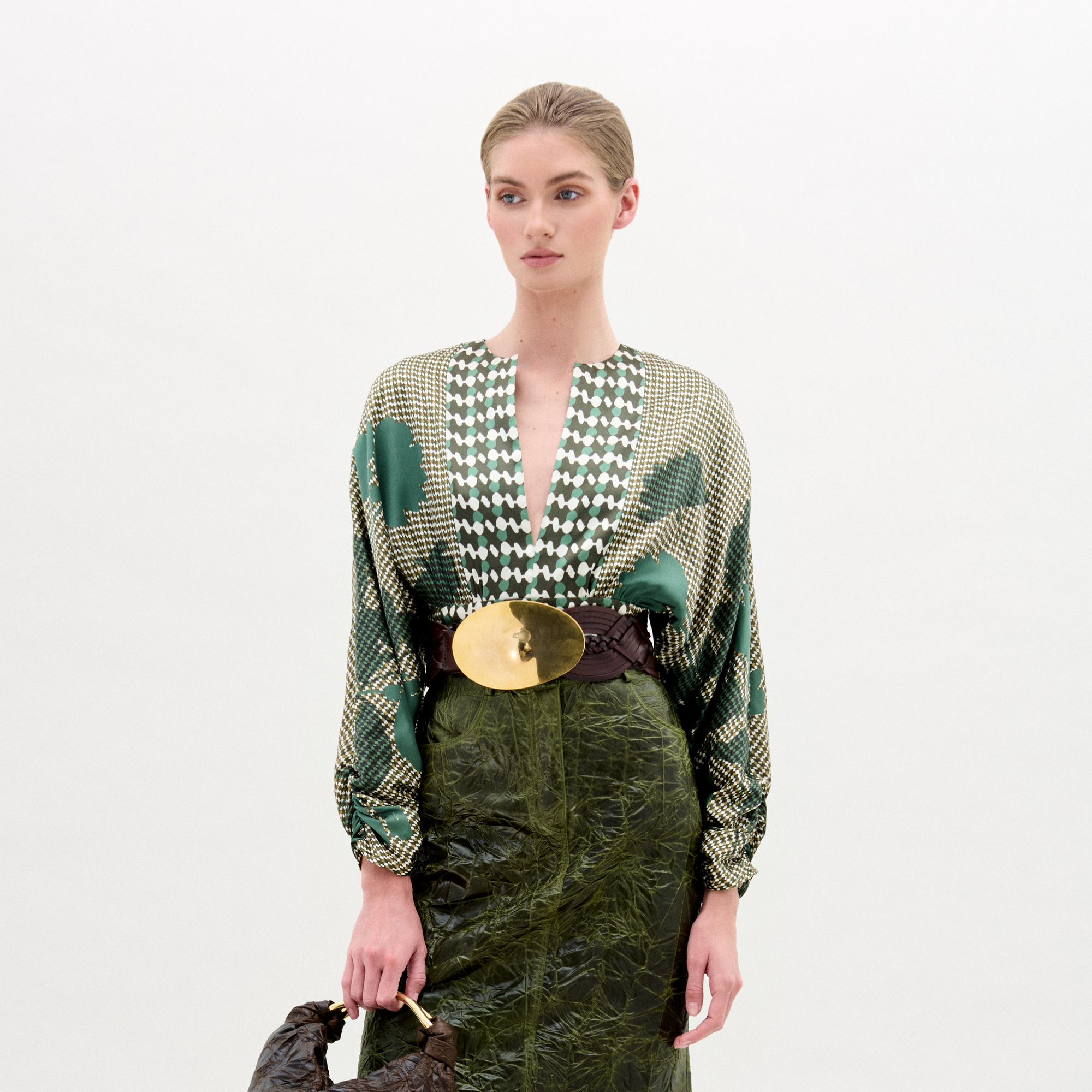 Model wearing a patterned top and green skirt with a white background