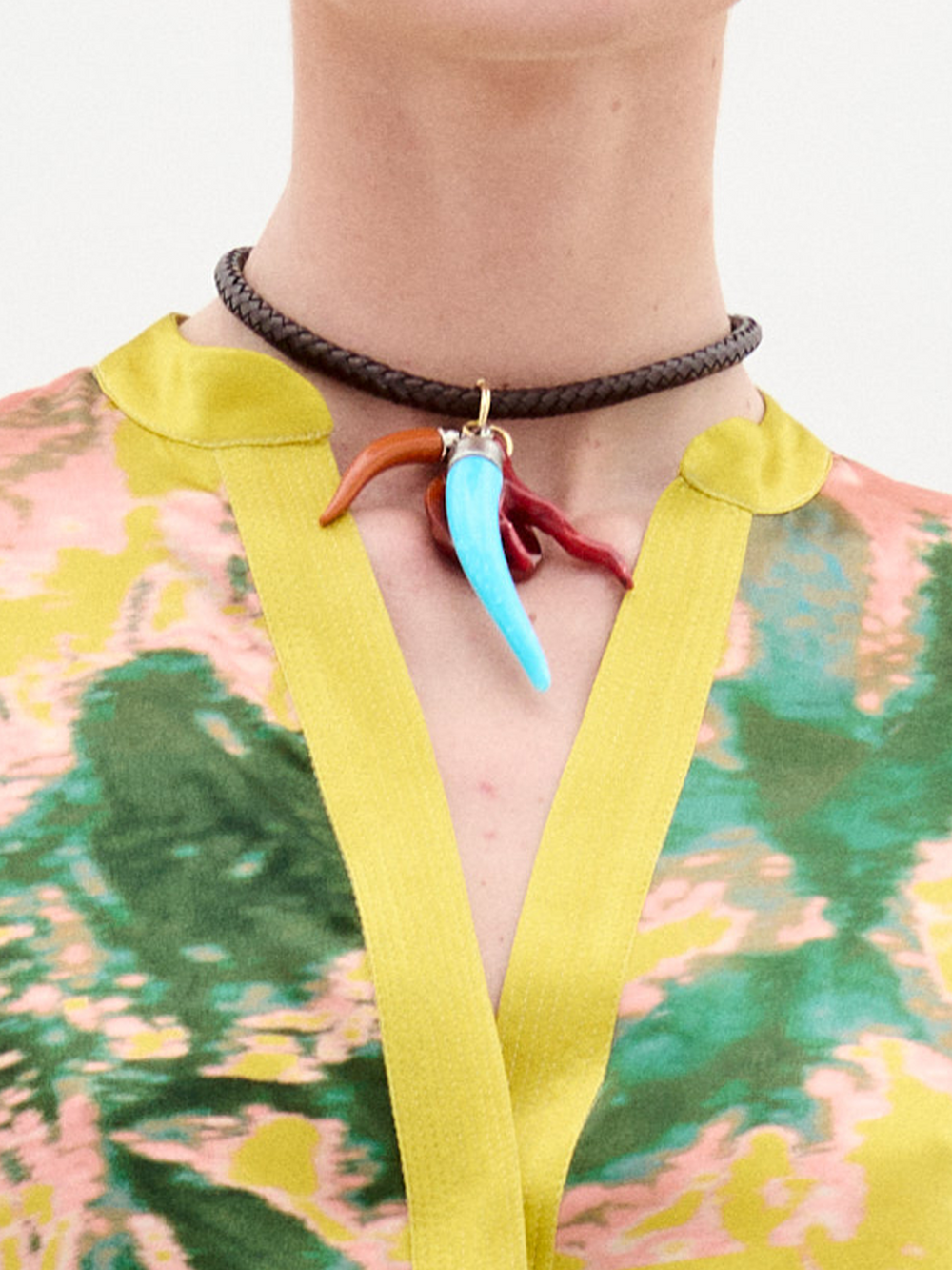A person wears the SVT DESIGNS Leslie Chocker, a braided leather necklace with three multicolor horn-shaped charms, paired with a colorful patterned top trimmed in yellow.