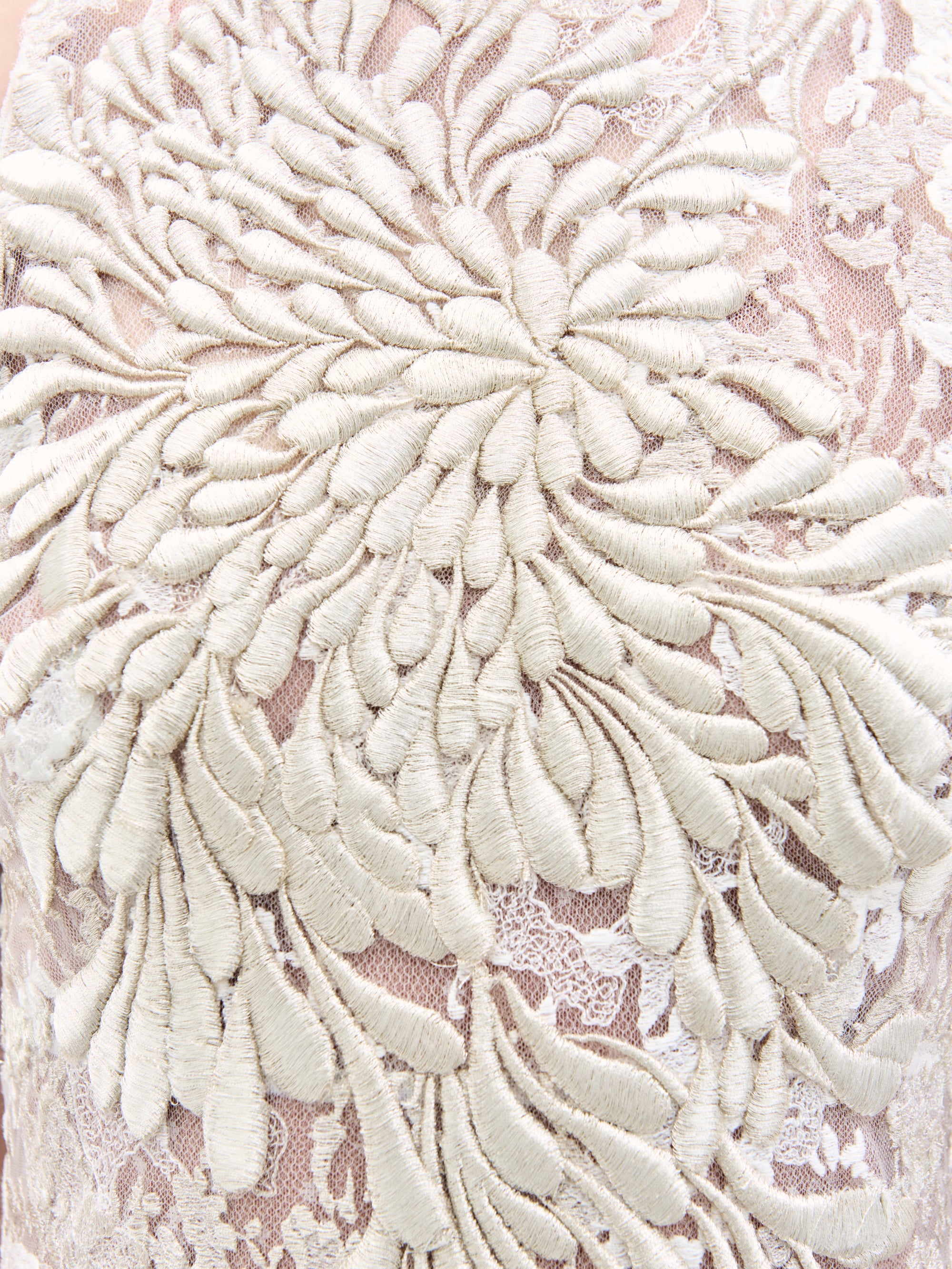 Close-up of intricate floral embroidery on the Levi Dress by SVT DESIGNS. Cream-colored threads create an elaborate raised flower pattern on a sheer, light fabric background, offering a rich and detailed texture.