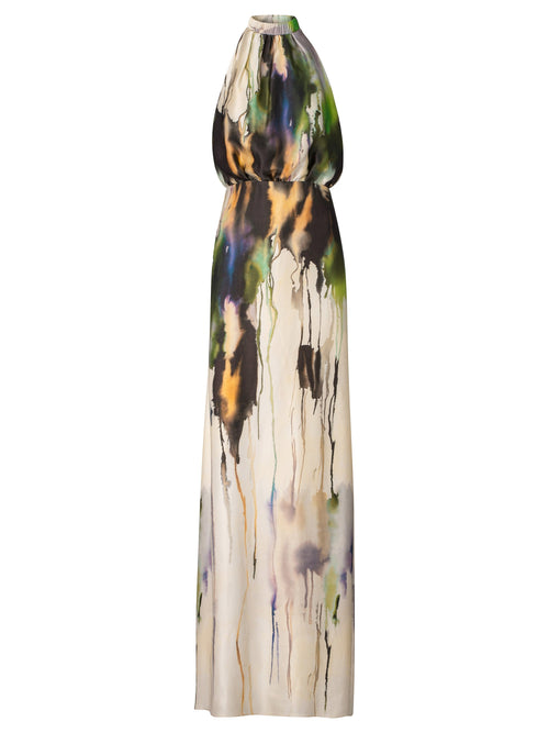 A woman in an elegant, long, Mabel Dress Olive Watercolor with an abstract design, available for pre-order, standing against a light blue background.