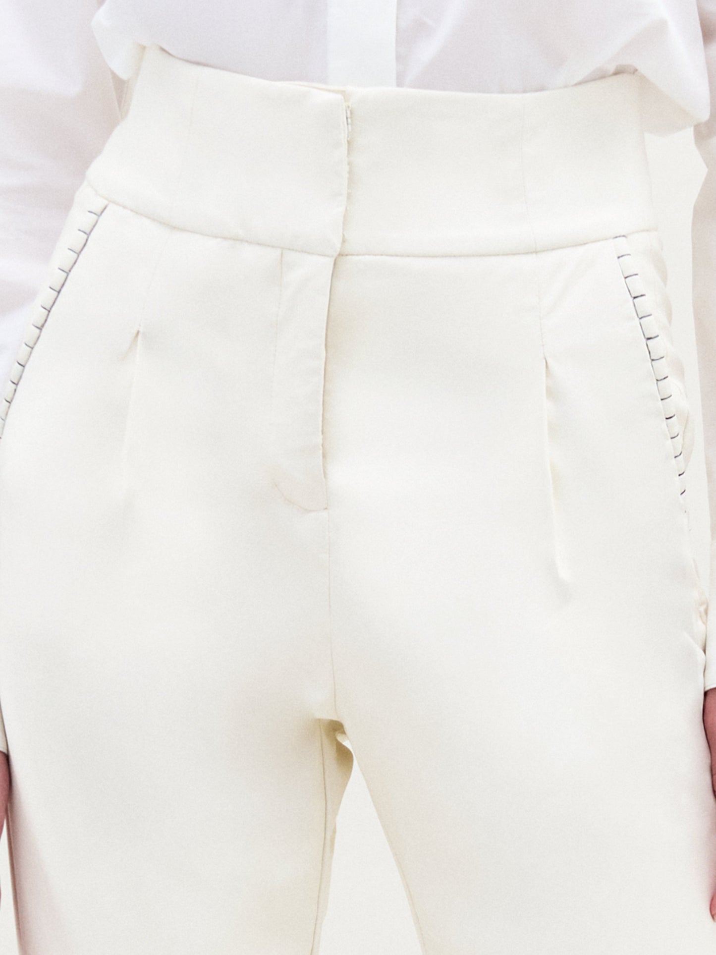 A person wears SVT DESIGNS' Moad Pant, a cream high-waisted cropped pant crafted from Italian fabric. It features pleats, visible stitching by the pockets, and straight fitted legs. The white shirt is neatly tucked in.