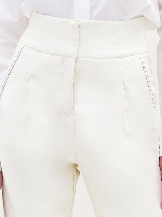 A person wears SVT DESIGNS' Moad Pant, a cream high-waisted cropped pant crafted from Italian fabric. It features pleats, visible stitching by the pockets, and straight fitted legs. The white shirt is neatly tucked in.