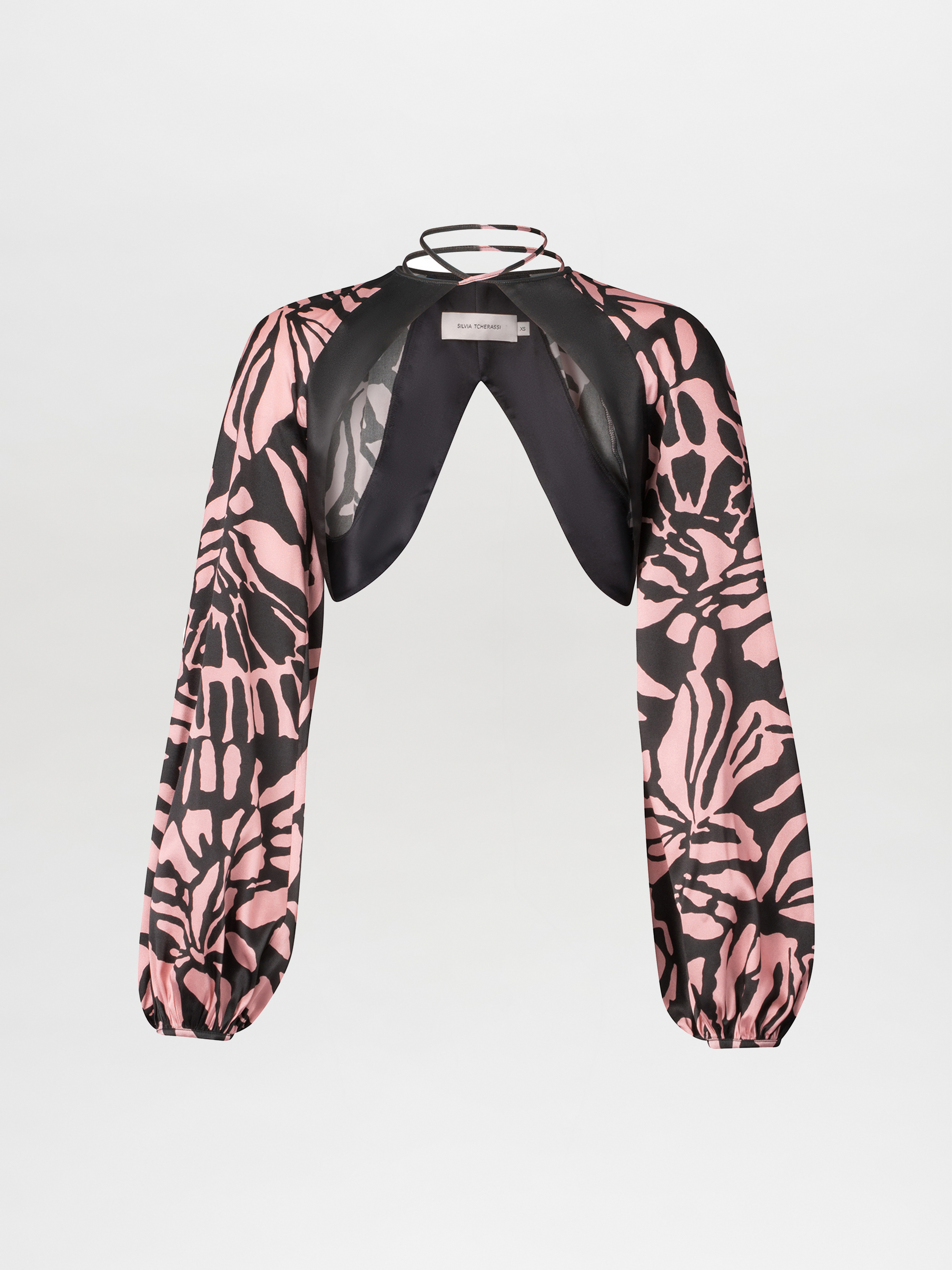 The Moira Cape by SVT DESIGNS is a pink and black abstract print long-sleeve cropped blouse with an open front, gathered cuffs, and a black halter neckline with visible straps, shown on a white background.