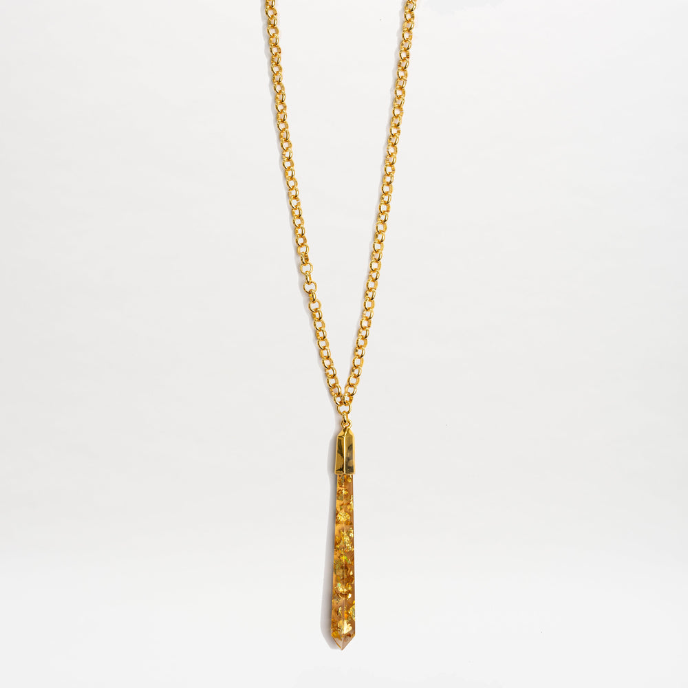 The Montse Necklace by SVT DESIGNS features a gold chain and a geometric crystal pendant with amber-colored stones, showcased against a plain white background.