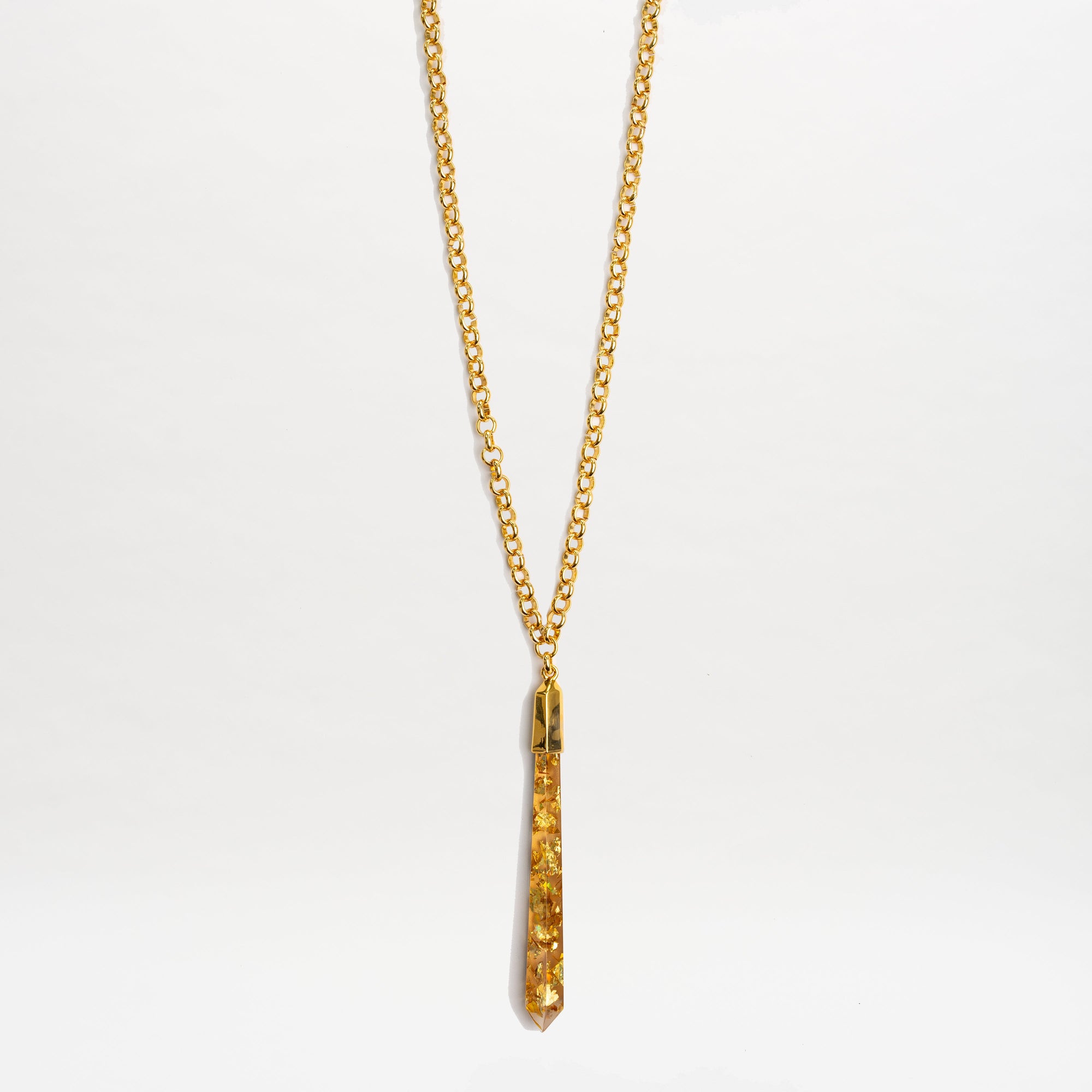 The Montse Necklace by SVT DESIGNS features a gold chain and a geometric crystal pendant with amber-colored stones, showcased against a plain white background.