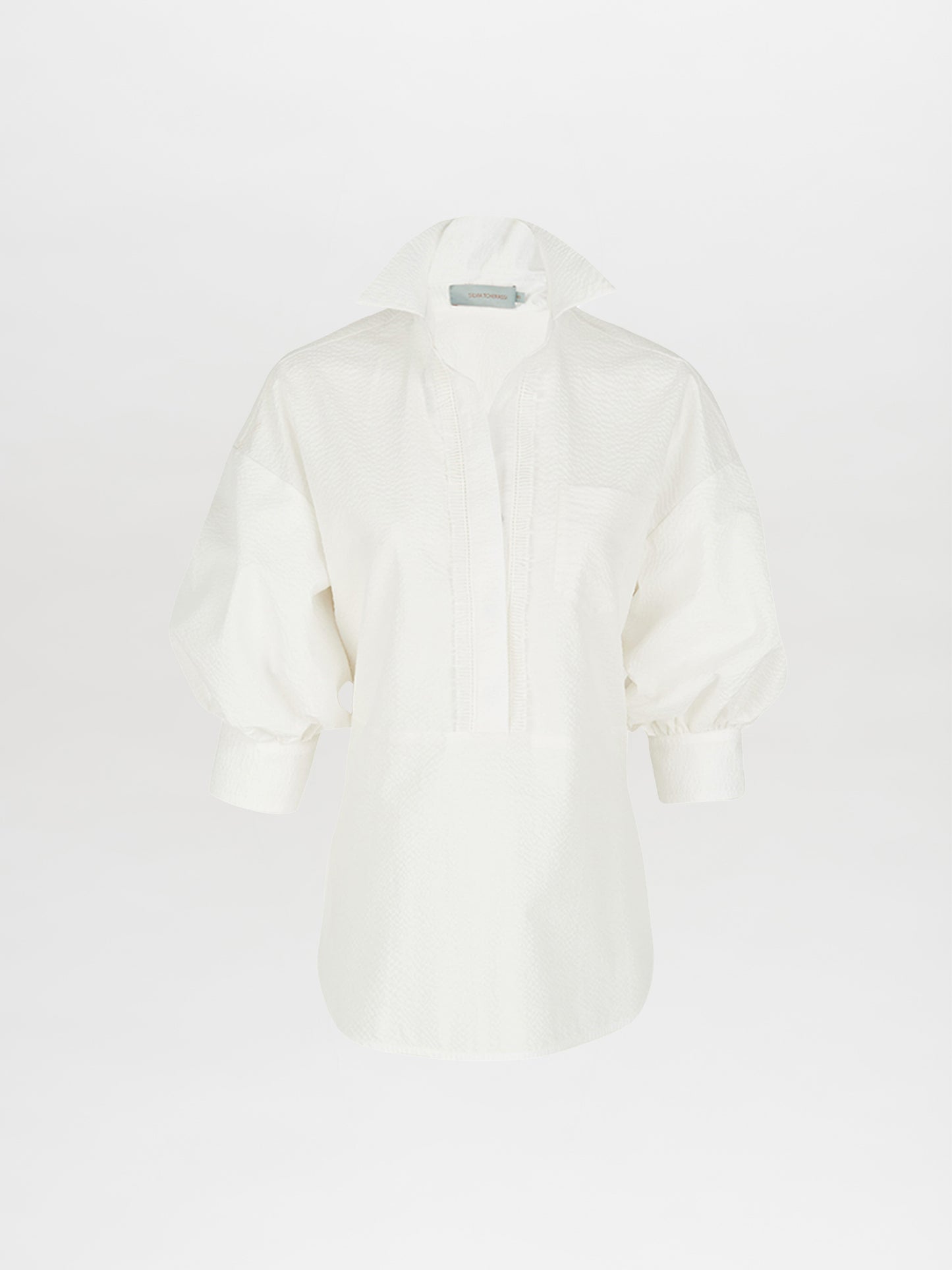 The Silvia Tcherassi Manrola Blouse in white features a deep V-neck, short collar, wide long sleeves, and a textured pattern against a plain white background.