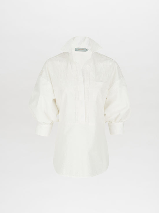 The Silvia Tcherassi Manrola Blouse in white features a deep V-neck, short collar, wide long sleeves, and a textured pattern against a plain white background.