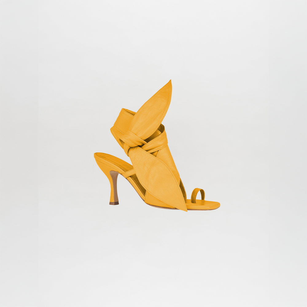 The Marco Heel Yellow by Silvia Tcherassi is a high-heeled sandal in bright yellow Italian calf leather, featuring a sculptural silhouette with large, pointed leaf-like shapes wrapping the foot, shown against a plain white background.