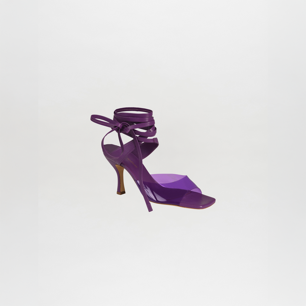 The Marlene Heels are purple high-heeled sandals made from luxurious Italian calf leather, featuring tie-around ankle straps, shown against a plain white background.