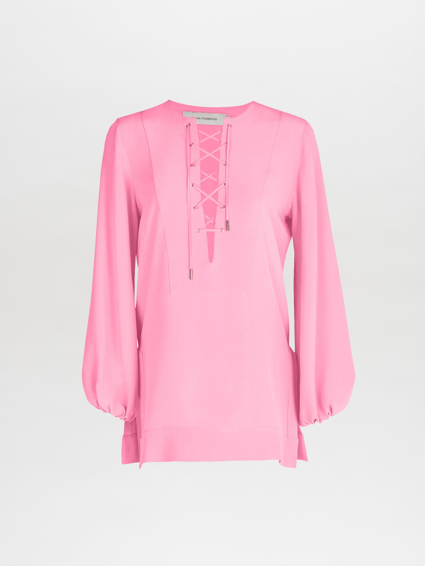 The Merve Blouse by Silvia Tcherassi features a v-shaped lace-up neckline and long, loose sleeves in pink silk, exuding casual glamour against a plain white background.