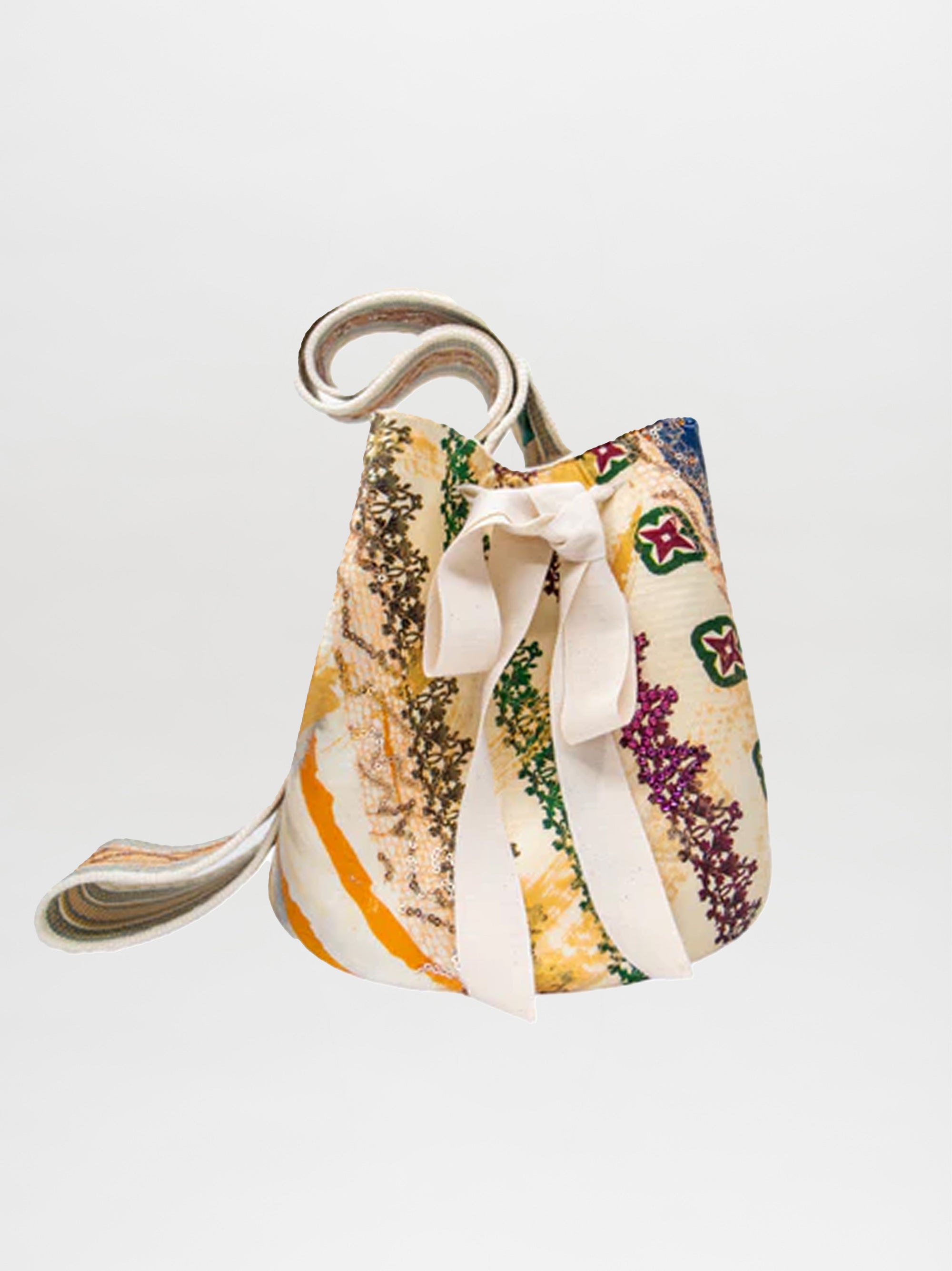 The Mochila Laaput Honey handbag by SilviaTcherassiEU is displayed on a plain white background, highlighting its Wayuu craftsmanship with vibrant green, yellow, red, and orange patterns. It's adorned with a large white bow and has a multicolored hand-woven strap extending from the top.